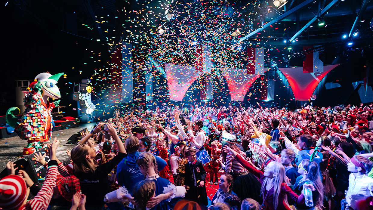 Das Maskottchen des Kinderkarnevals "Jecko" sthet auf einer Bühne vor Publikum.